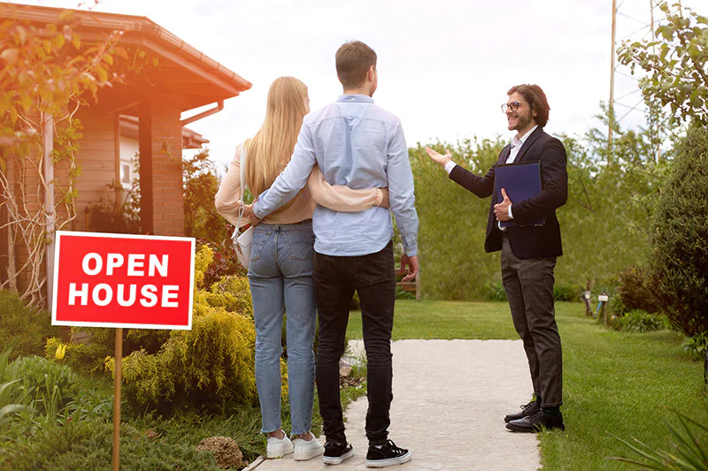 real estate agent showing open house to young couple outdoors